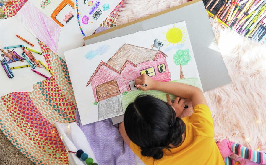 Girl coloring photo of home on rug.