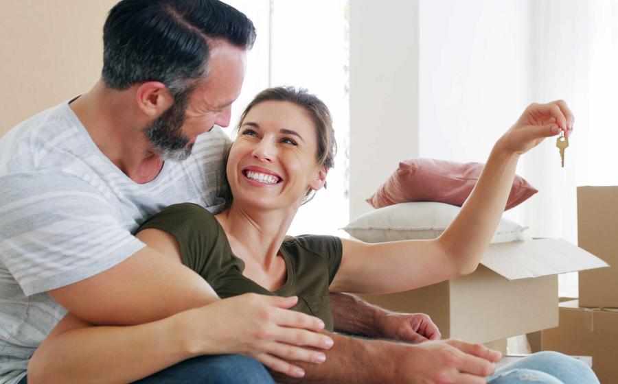 Happy middle-aged couple sitting on floor near moving boxes holding keys