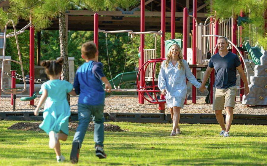 Two children running toward smiling parents at a community park. 