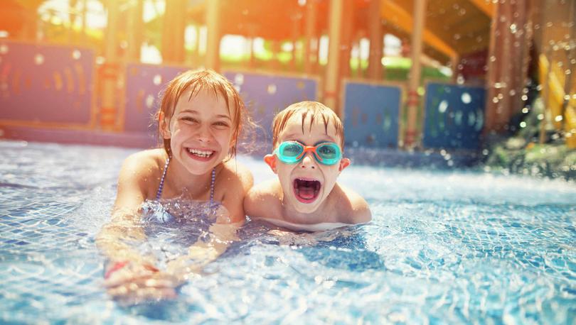 Brother and big sister swimming at water park with rides in the background.