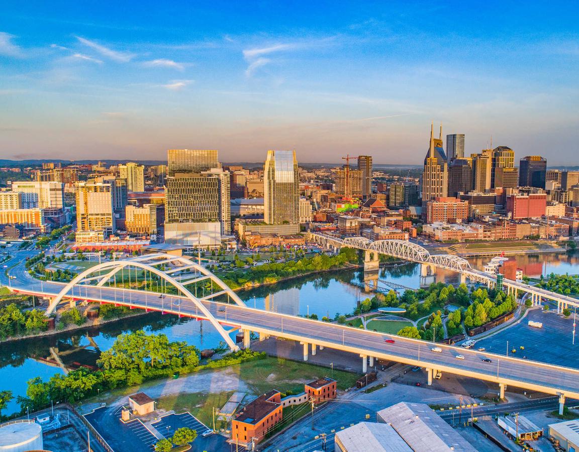 Nashville, Tennessee skyline showing bridges crossing the Cumberland River, downtown city buildings, and blue skies on the horizon