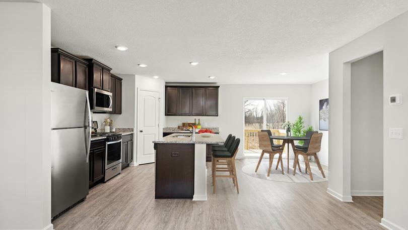 Photo of spacious kitchen with an island, stainless steel appliances, plank flooring and an adjacent dining area with a sliding glass door.