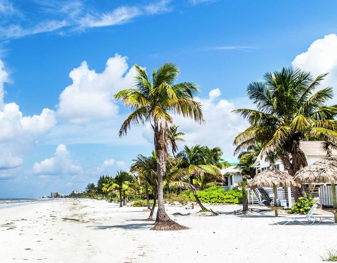 Fort Myers, Florida beach with white sands, palm trees, and bright blue, cloudy skies in the distance