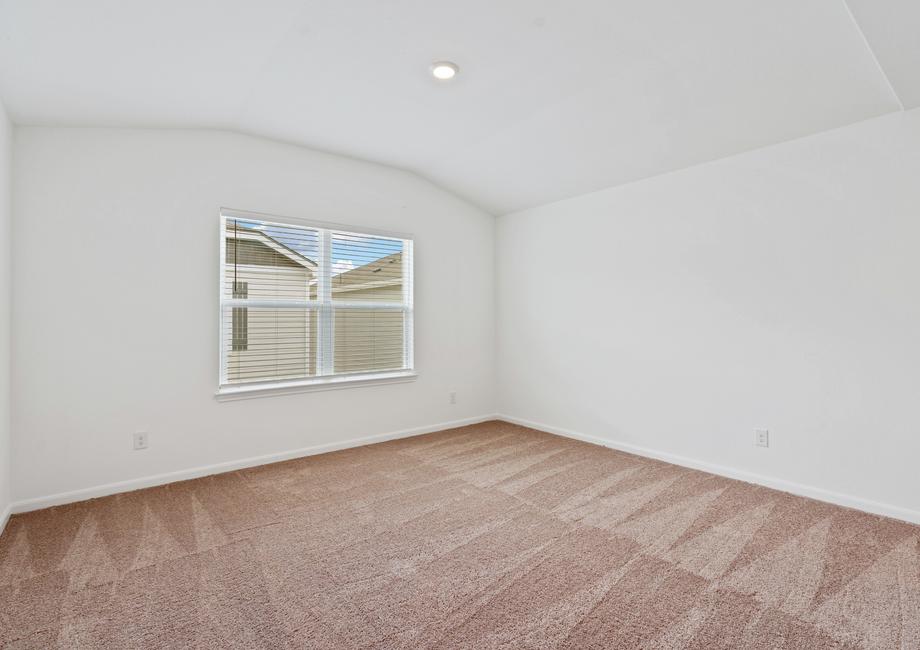 Master bedroom with a vaulted ceiling, tan carpet, and a large window.