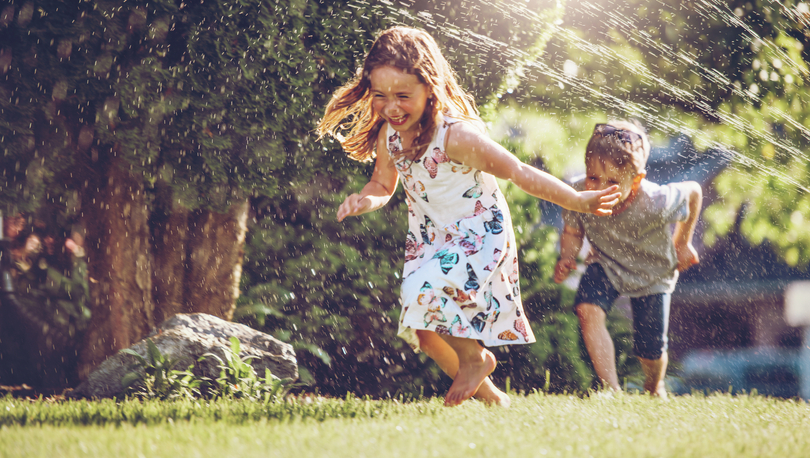 Kids running through sprinklers in a yard.