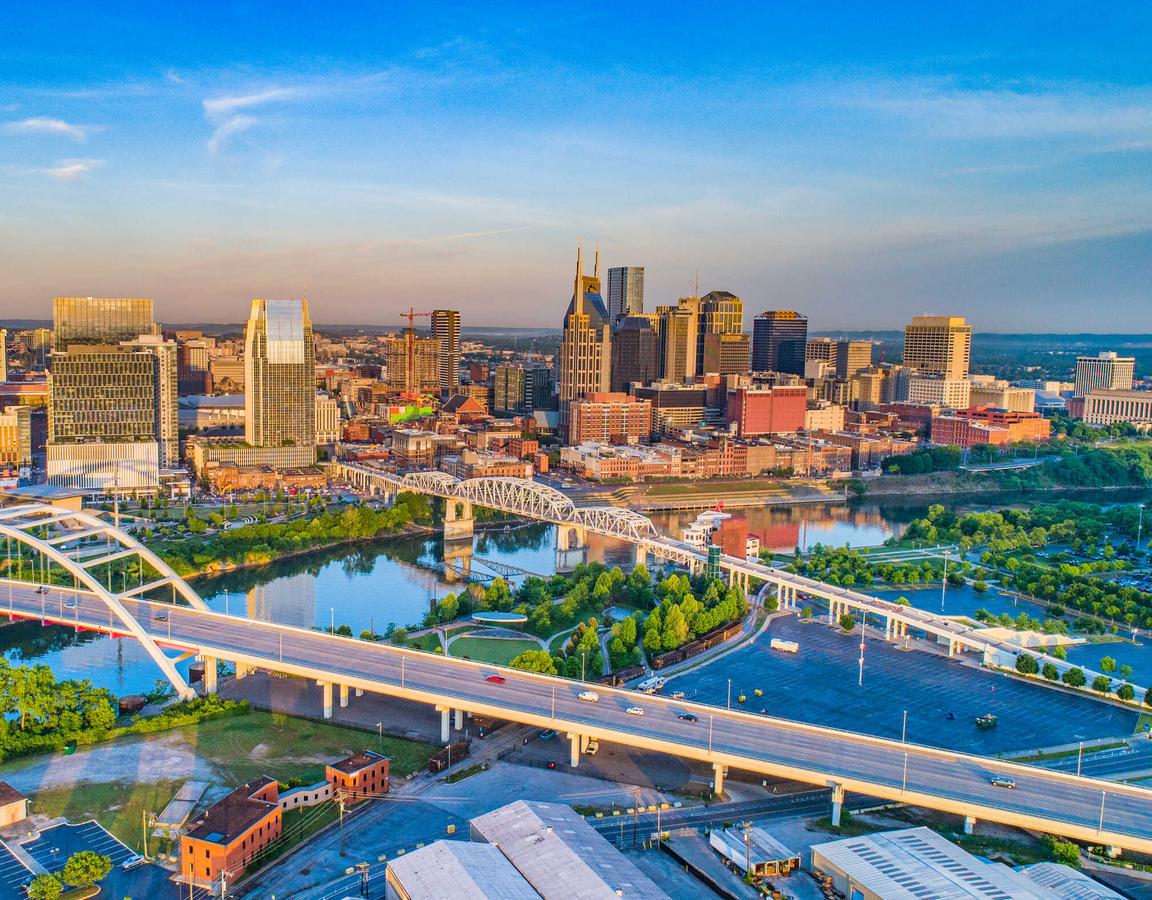 Nashville, Tennessee cityscape taken from across the Cumberland River showing flowing water, green grass, and tall office buildings in the distance