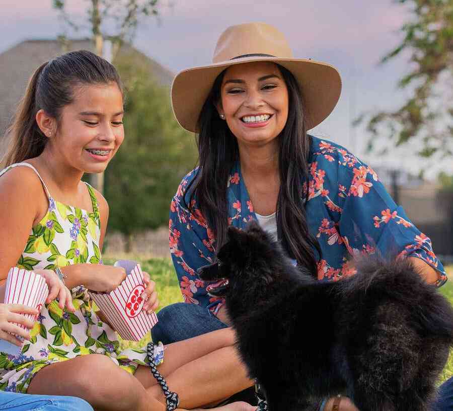 Smiling family sitting down on a field with a small dog. 