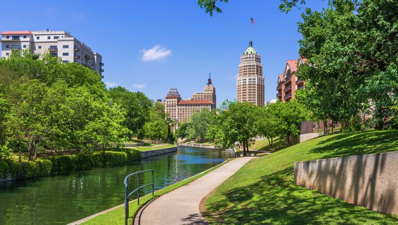 San Antonio, Texas Riverwalk during the day showing walking trails, trimmed green grass, and office buildings in the distance