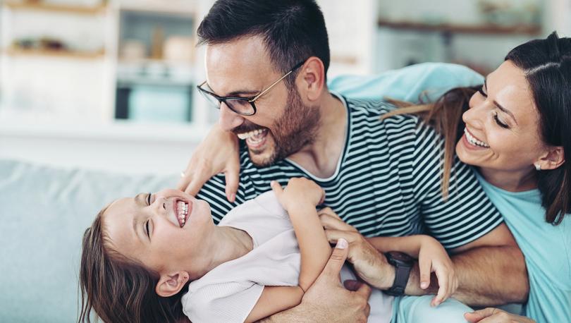 Stock photo of two parents playing with a little girl at home.