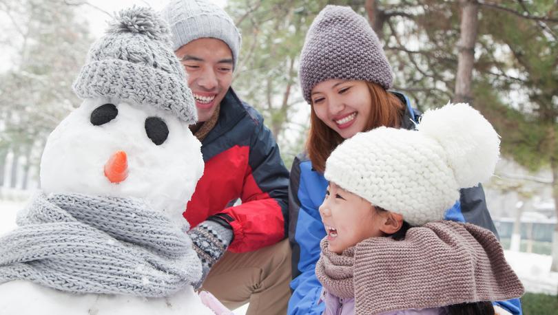 Family making snowman in a park in the winter.