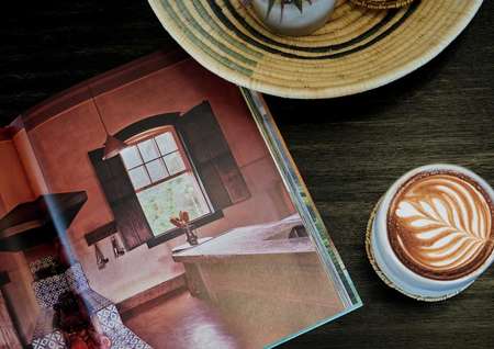 A wooden coffee table with a home decor book opened and a fresh latte in a mug next to it.