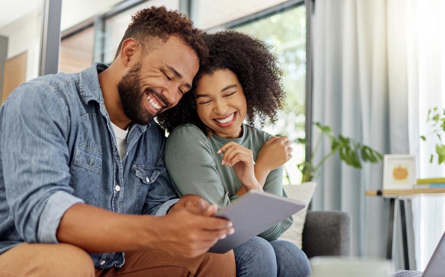 Young happy couple going through documents and using a digital tablet at a table together at home.