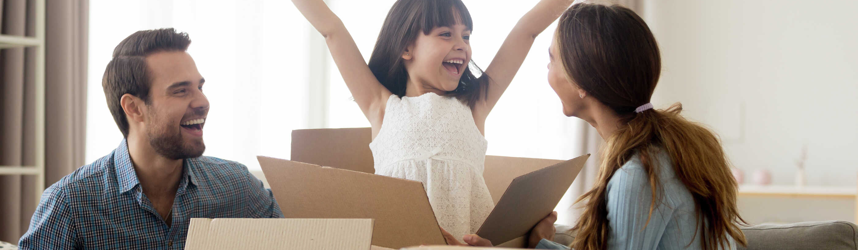 Stock image of family unpacking boxes, little girl excited with hands in the air.