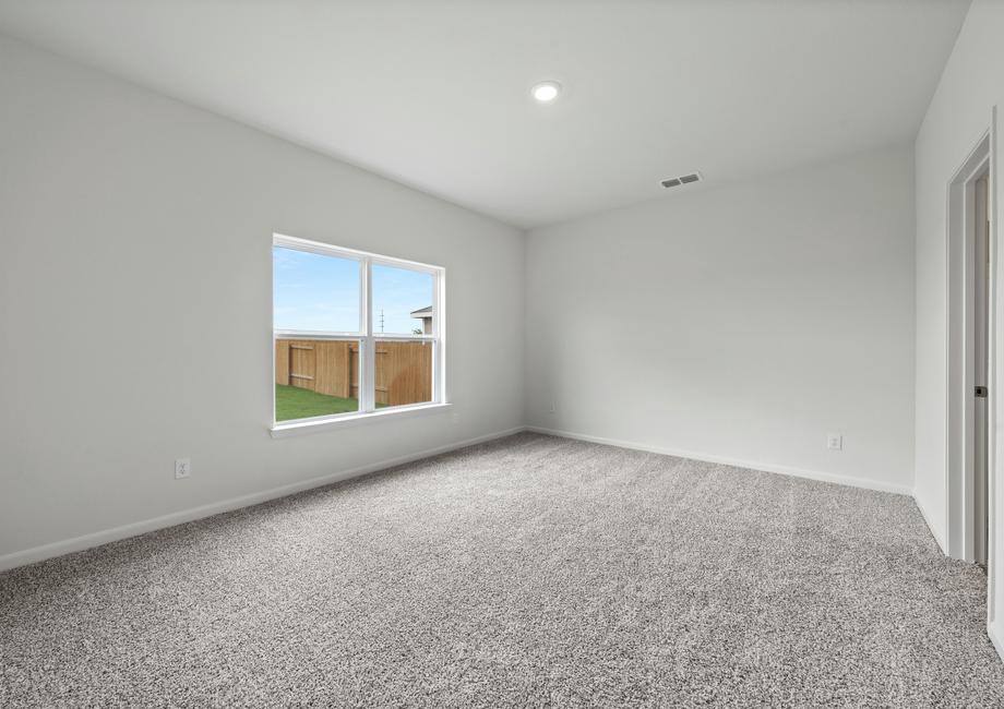 The large master bedroom of the Driftwood has a large window with backyard views.