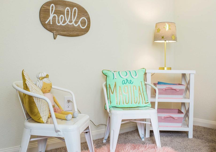Kid's playroom with wooden sign on the wall, two kid's chairs with pillows and a shelf with lit lamp in the corner.