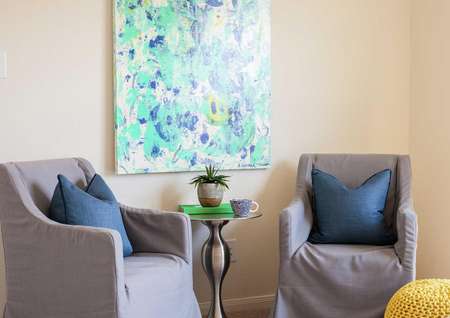 Living room completed with gray sofa and chair, round end table with a plant sitting on it and a blue abstract painting on the wall.