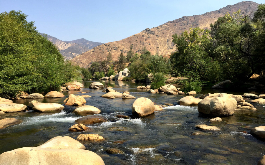 Bakersfield, California Kernville Kern River with large boulders throughout the river, trees lining the banks, and mountains in the distance