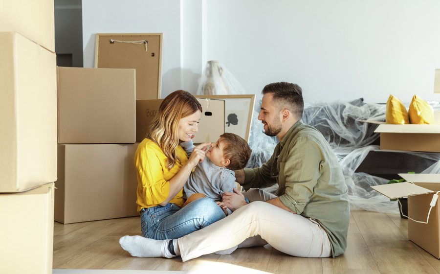 Couple sitting on the floor of their new home with their son between them.