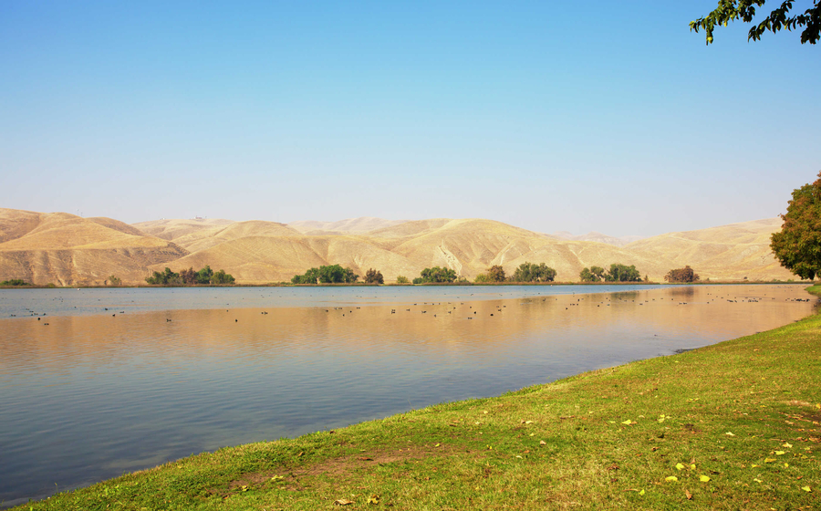Bakersfield, California Lake Ming man-made recreational area with calm waters, lined with green grass, and mountain ranges in the distance