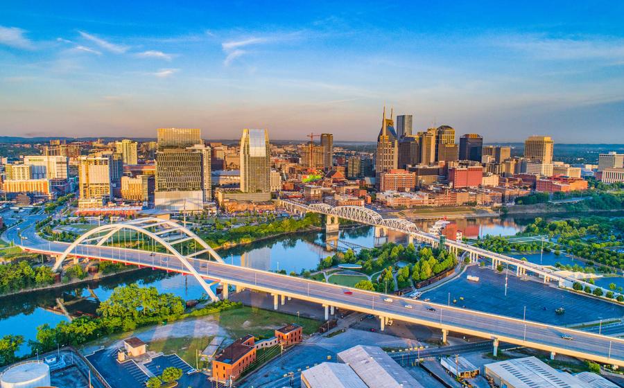 Nashville, Tennessee skyline showing bridges crossing the Cumberland River, downtown city buildings, and blue skies on the horizon