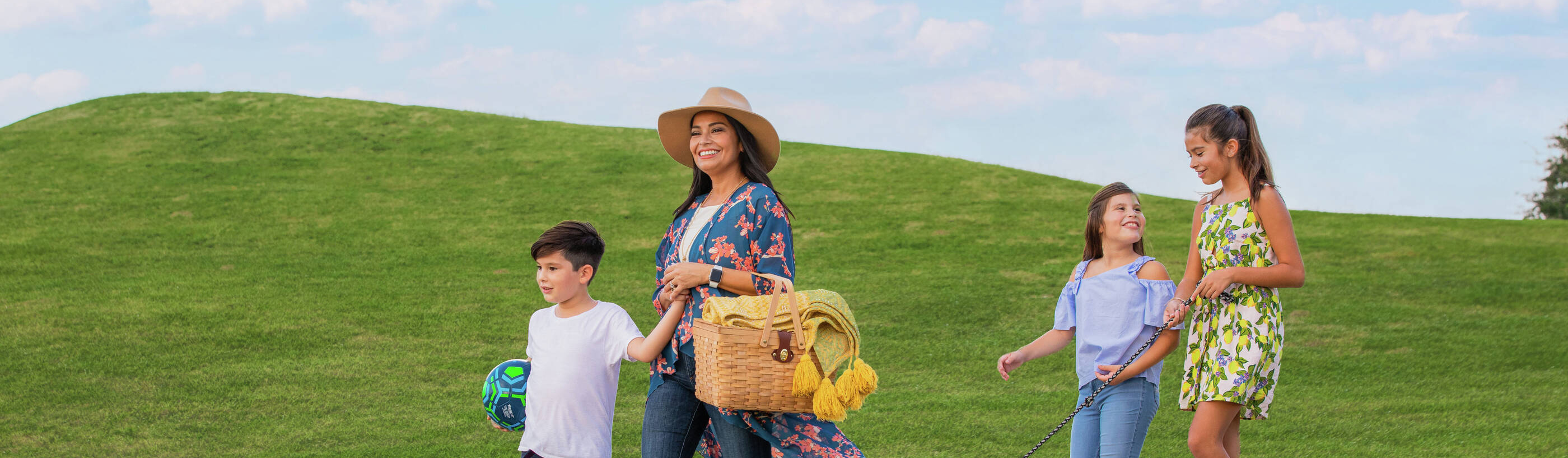 A family walking through the beautiful walking trails of a neighborhood with a picnic basket and their dog. 