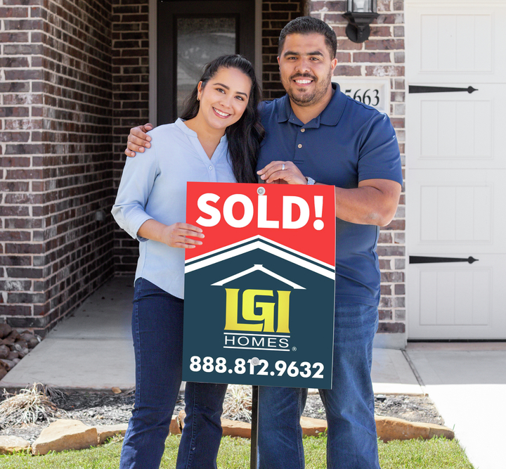 Couple standing in front of home with their sold sign