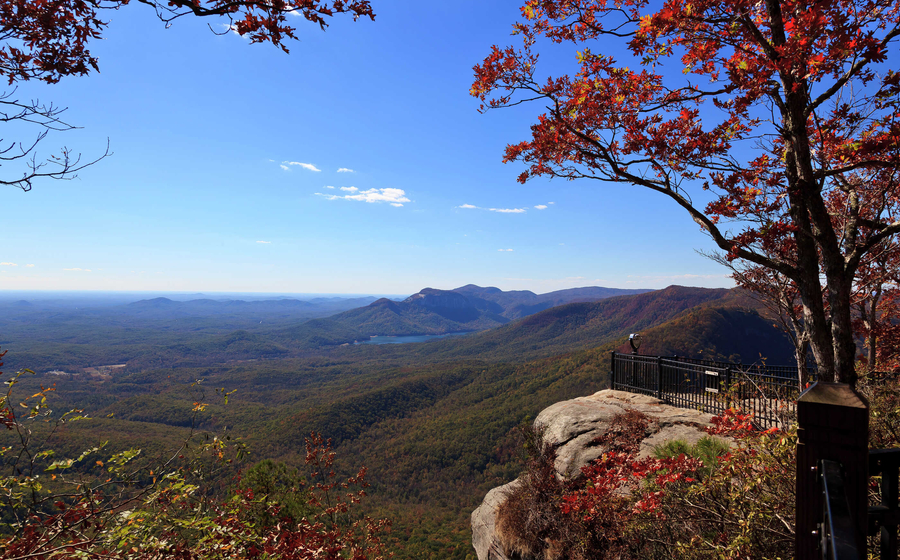 Mountains during Autumn showing woman sitting on rocky outcropping, trees that have lost their leaves, and rolling hills of vegetation