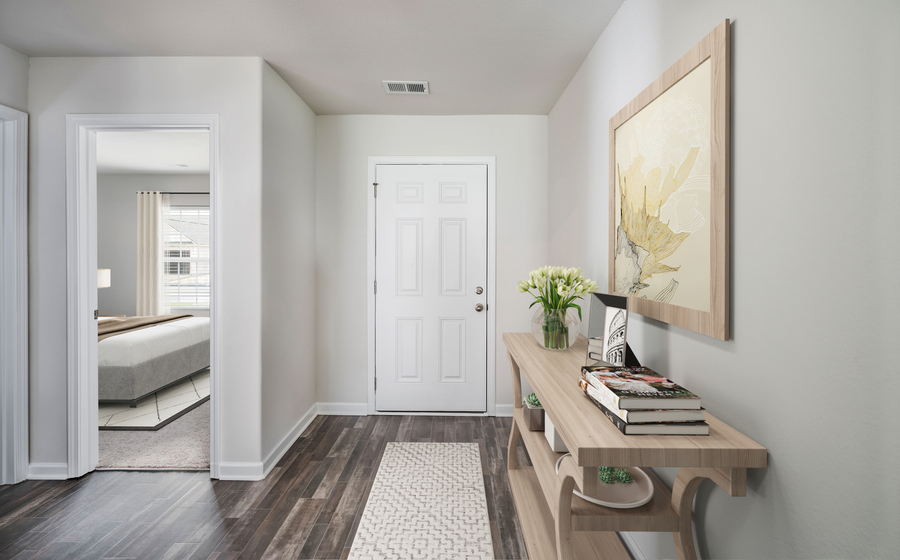 Staged entryway with rug and side table with view of secondary bedroom.