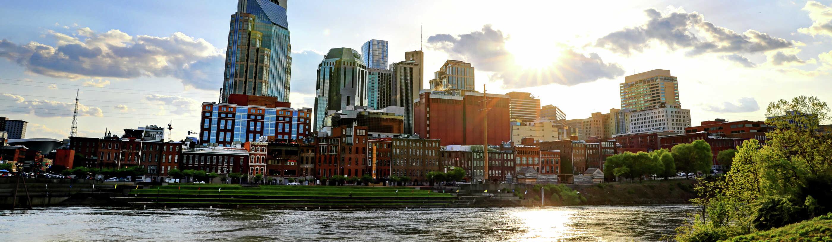 Nashville, Tennessee cityscape taken from across the Cumberland River showing flowing water, green grass, and tall office buildings in the distance