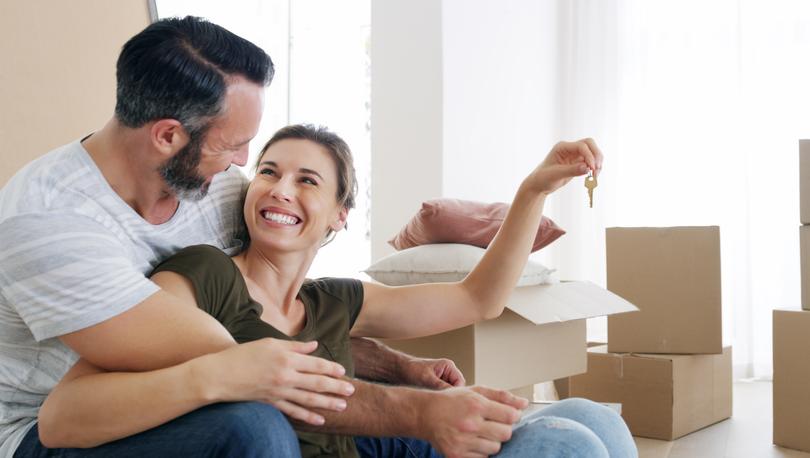 Happy middle-aged couple sitting on floor near moving boxes holding keys