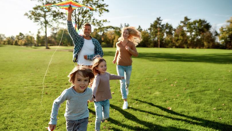 Family running in a field with a kite on a sunny day.