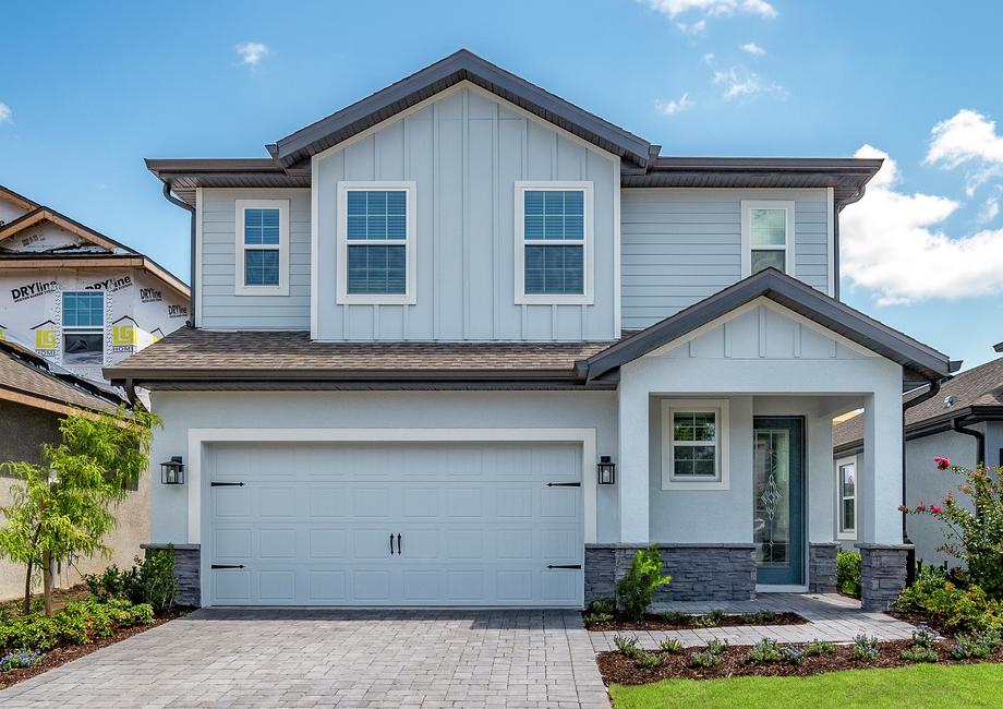 Large, two-story home with light blue paint, brown stone and beautiful flower beds.