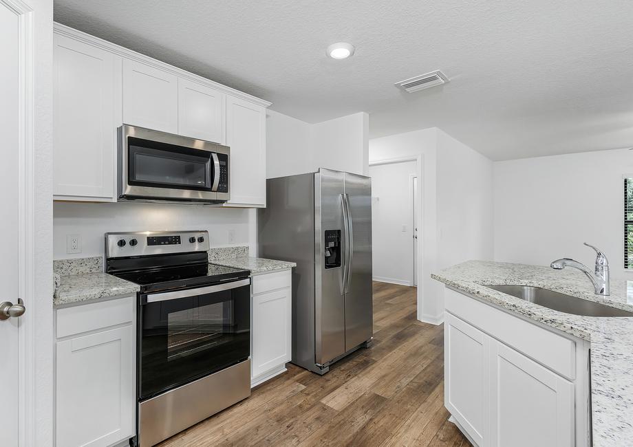 A kitchen with white granite countertops, white cabinets, and stainless steel appliances.