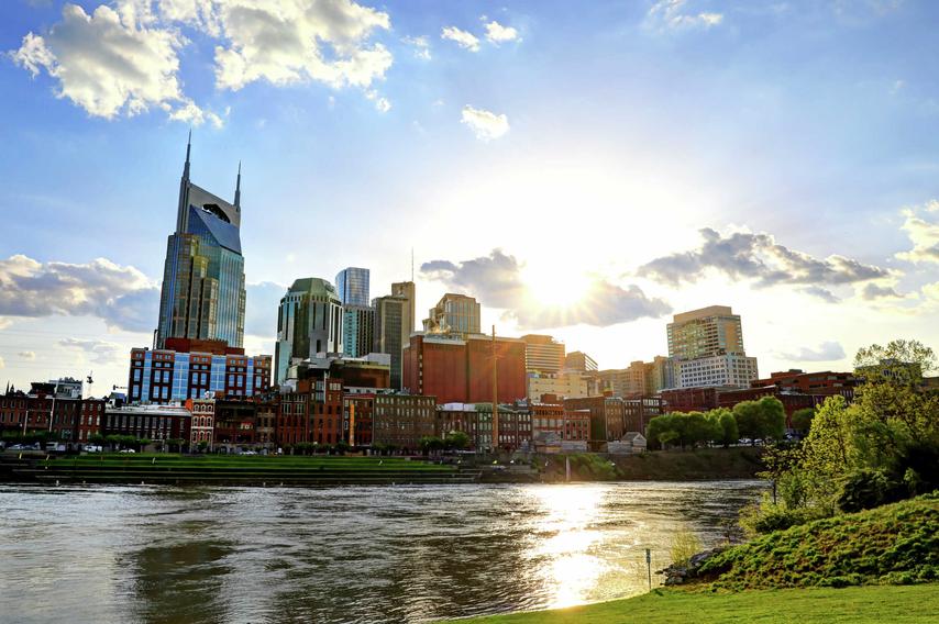 Nashville, Tennessee cityscape taken from across the Cumberland River showing flowing water, green grass, and tall office buildings in the distance