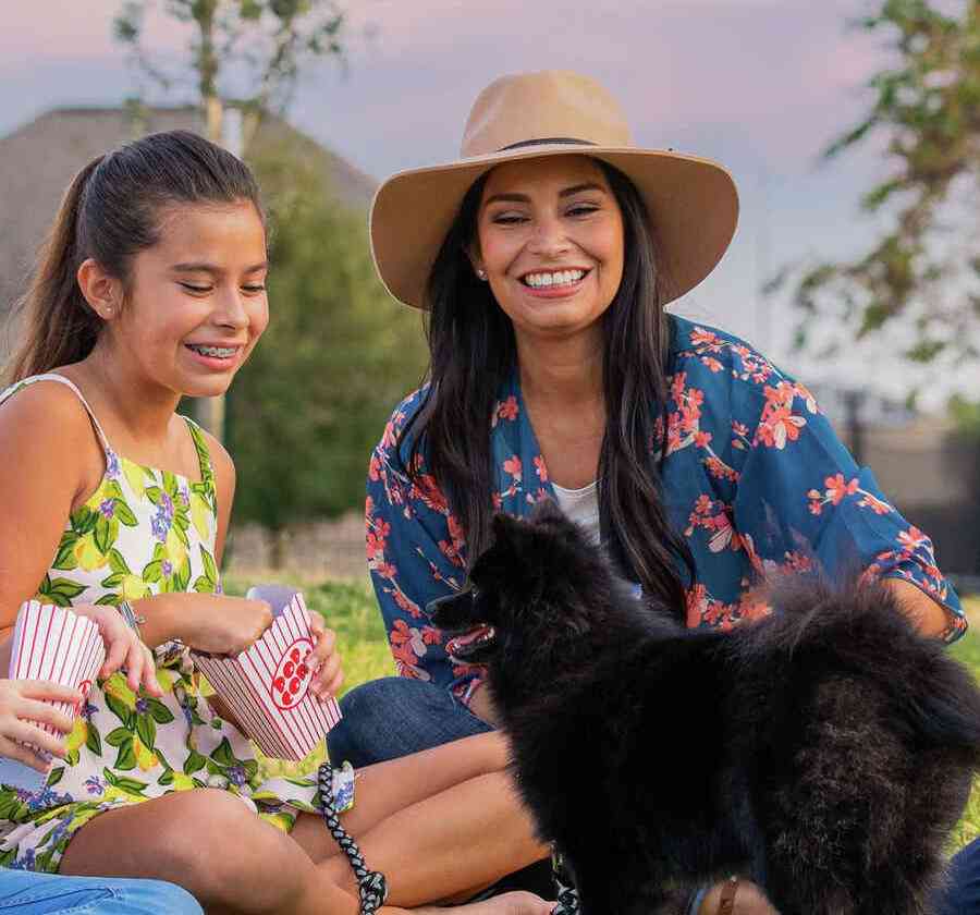 Smiling family sitting down on a field with a small dog. 