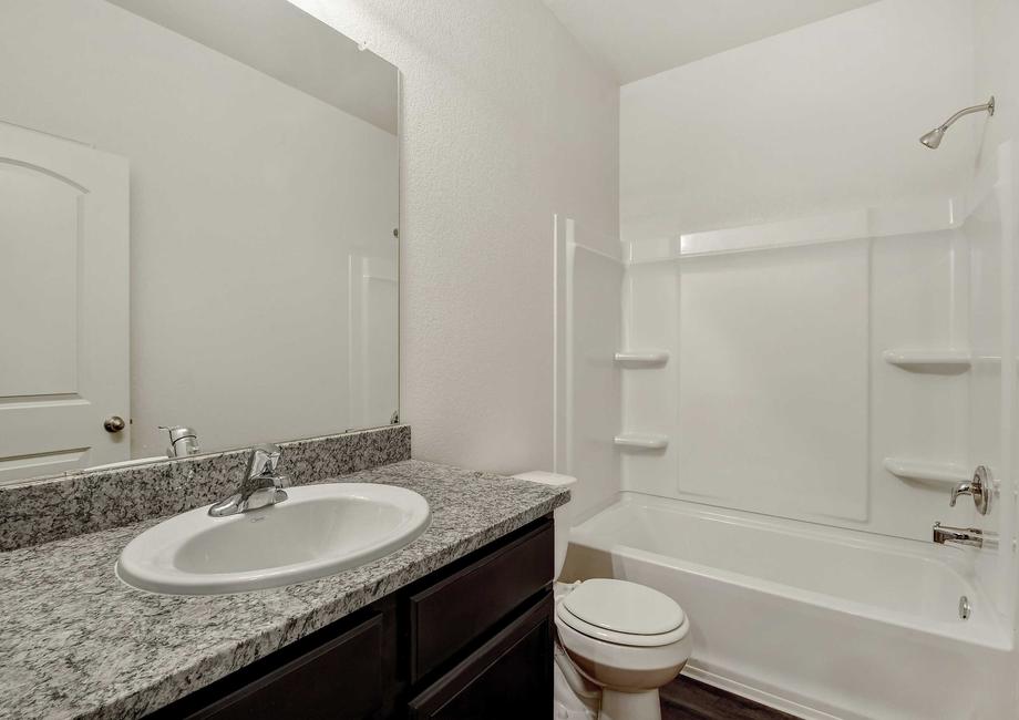 Kendall guest bathroom with white shower and bathtub unit, granite vanity with white sink, and white toilet