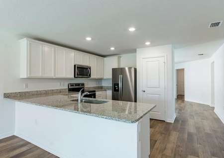 Open-concept kitchen with installed appliances, upper-wood cabinets and large granite countertops